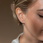 Close-up of a woman's ear wearing Opal Moon Mini Hoops—small gold huggie earrings with a crescent moon charm, ideal for an elegant stack or as part of your Opal Moon Earrings collection.