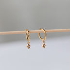 Ericka Diamond Huggies, featuring diamond-shaped hoops and dangling gemstone charms, hang delicately on a wooden stick.