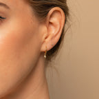 Close-up of a woman's ear wearing Ericka Diamond Huggies in 18K Gold alongside a tiny stud in the earlobe.