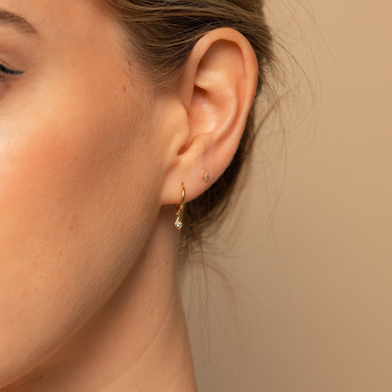 Close-up of a woman's ear wearing Ericka Diamond Huggies in 18K Gold alongside a tiny stud in the earlobe.
