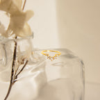 The Marina Chevron Ring, a delicate gold band with small diamonds, is displayed on a clear glass vase with dried flowers in gentle sunlight.