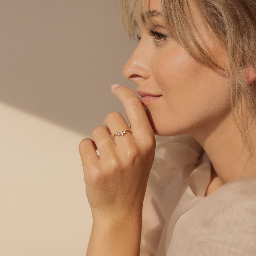 A woman in profile touches her lips, soft sunlight highlighting her face and hand adorned with the Marina Chevron Ring's delicate band.