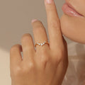 A hand adorned with the Marina Chevron Ring, showcasing three small diamonds on a delicate gold band, held near the lips against a soft neutral background.