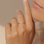 A hand adorned with the Marina Chevron Ring, showcasing three small diamonds on a delicate gold band, held near the lips against a soft neutral background.