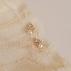 The Angelina Pearl Studs, featuring elegant pearls with gold and diamonds and a secure screw back design, are displayed on a textured cream-colored fabric background.