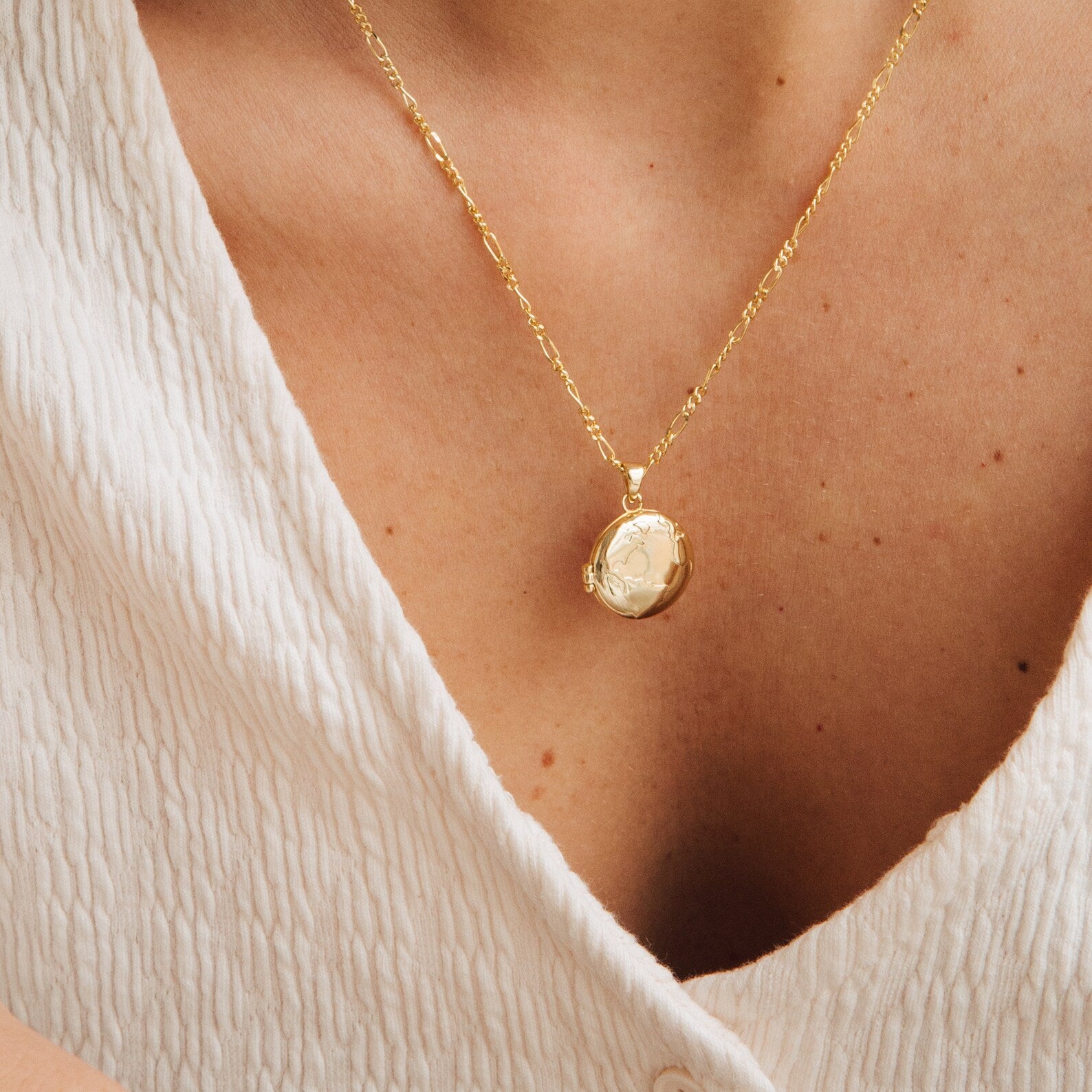 A person wearing a textured white top and the Endless Love Locket Necklaces, featuring a gold keepsake round photo locket pendant.