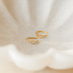 Amaya Marquise Threaders—gold earrings with small crystals, displayed on a textured cream shell background. Perfect for fans of dainty diamond clusters or elegant jewelry.