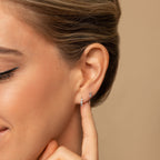 A woman smiles and points to the Amaya Marquise Threaders in her ear against a beige background, highlighting her elegant jewelry.
