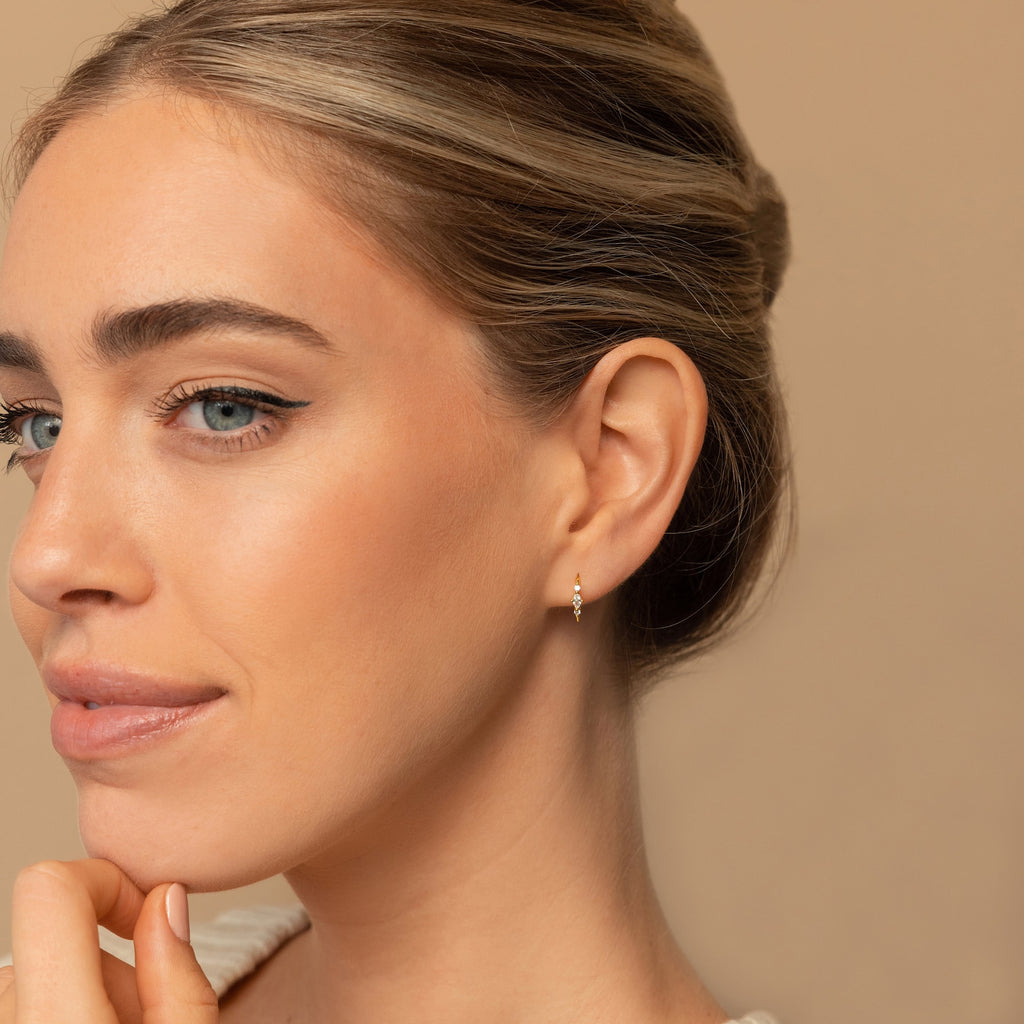 A woman with light eyes and smooth skin wears the elegant Amaya Marquise Threaders, looking thoughtful against a beige background.