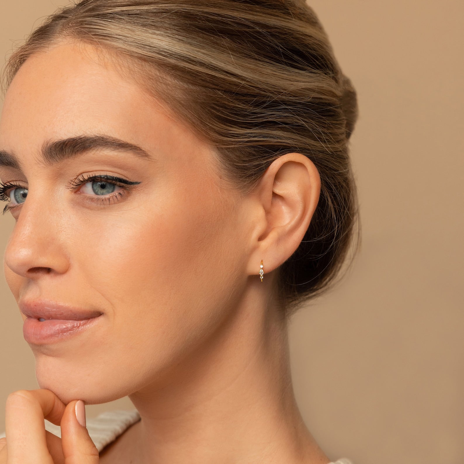 A woman with light eyes and smooth skin wears the elegant Amaya Marquise Threaders, looking thoughtful against a beige background.