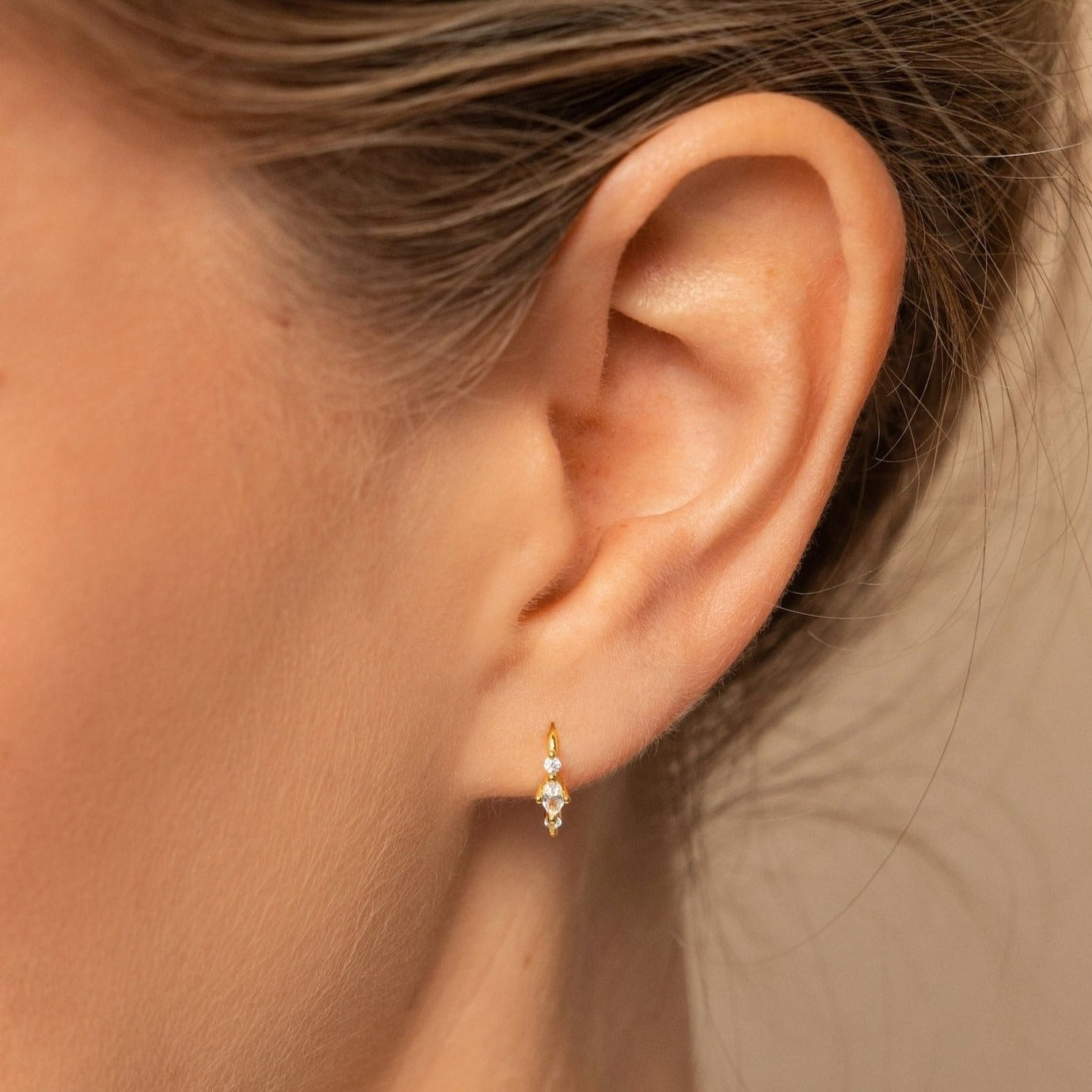 Close-up of a woman's ear wearing the Amaya Marquise Threaders, elegant gold earrings featuring a dainty diamond cluster with two sparkling gemstones.