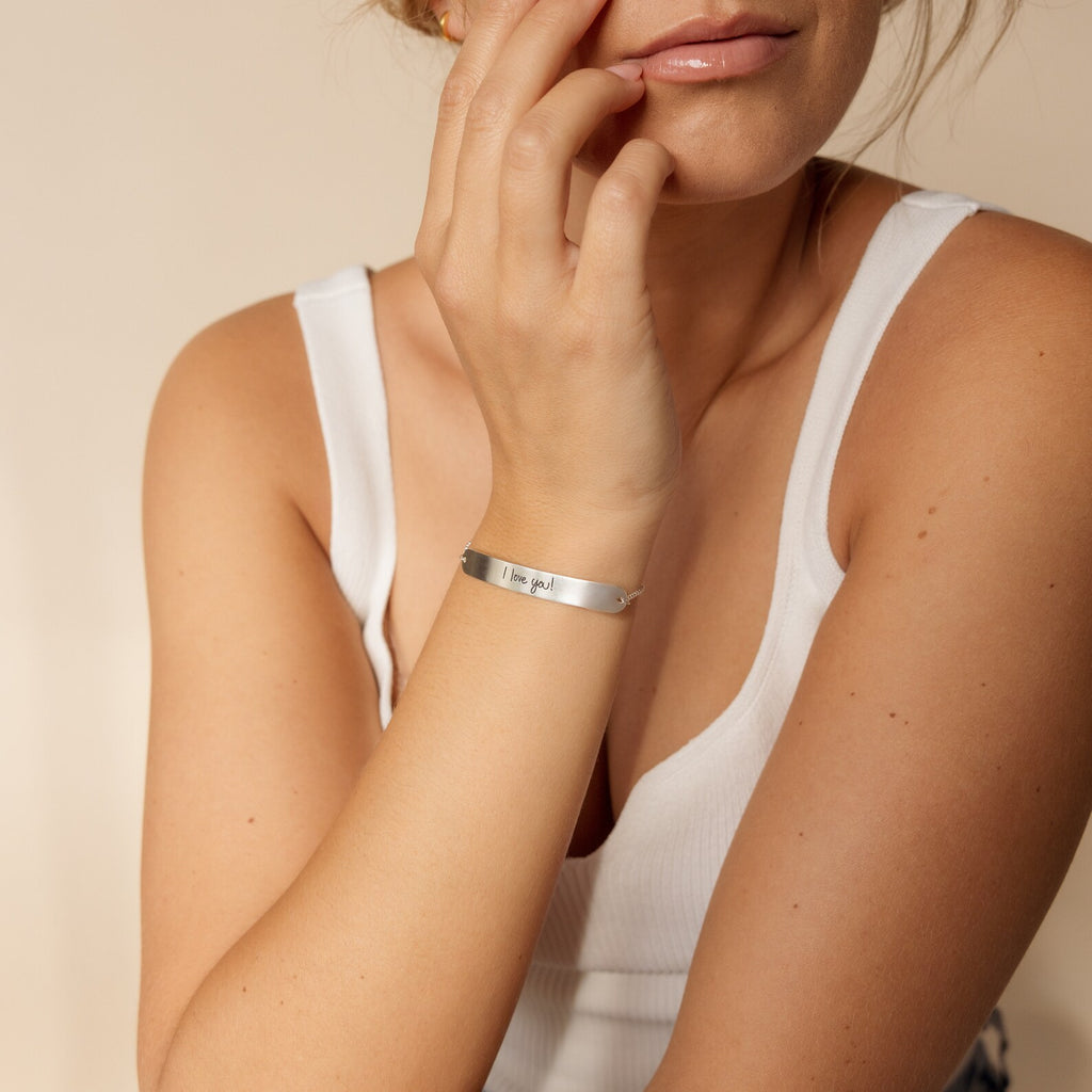 Woman wearing a white tank top and the delicate Slider Handwriting Bracelet, touching her face gently.