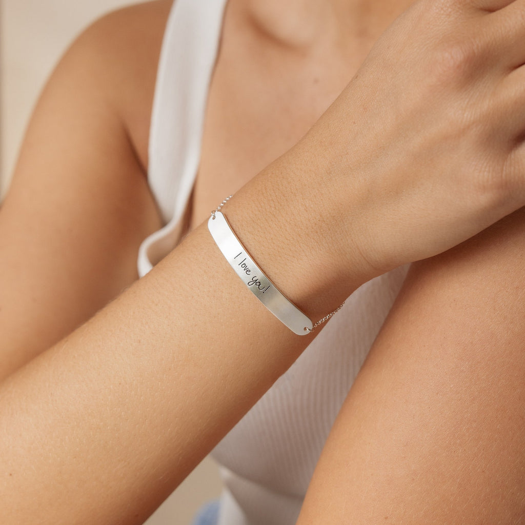 A person wears the Slider Handwriting Bracelet in silver, engraved with "I love you," paired with a white sleeveless top.