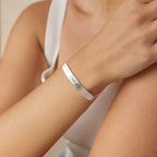 A person wears the Slider Handwriting Bracelet in silver, engraved with "I love you," paired with a white sleeveless top.