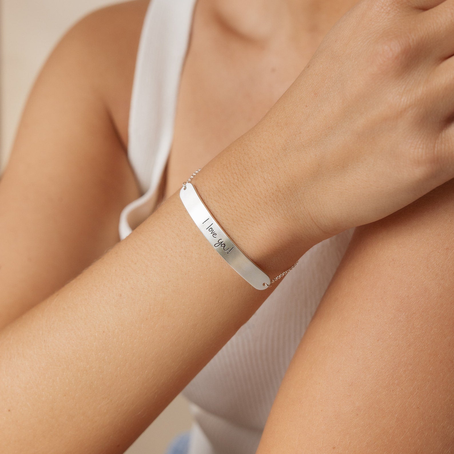 A person wears the Slider Handwriting Bracelet in silver, engraved with "I love you," paired with a white sleeveless top.