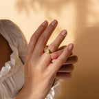 A person wearing a Pet Signet Ring with custom engraving gently touches their hands, illuminated by soft lighting against a beige background.