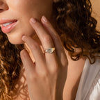 A woman with curly hair touches her face, wearing a gold Pet Signet Ring on her finger.