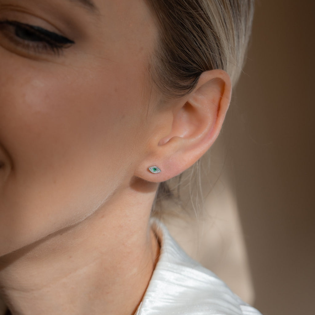 Close-up of a woman’s ear wearing Haven Emerald Eye Studs—small green emerald stone earrings—with part of her smiling face visible.