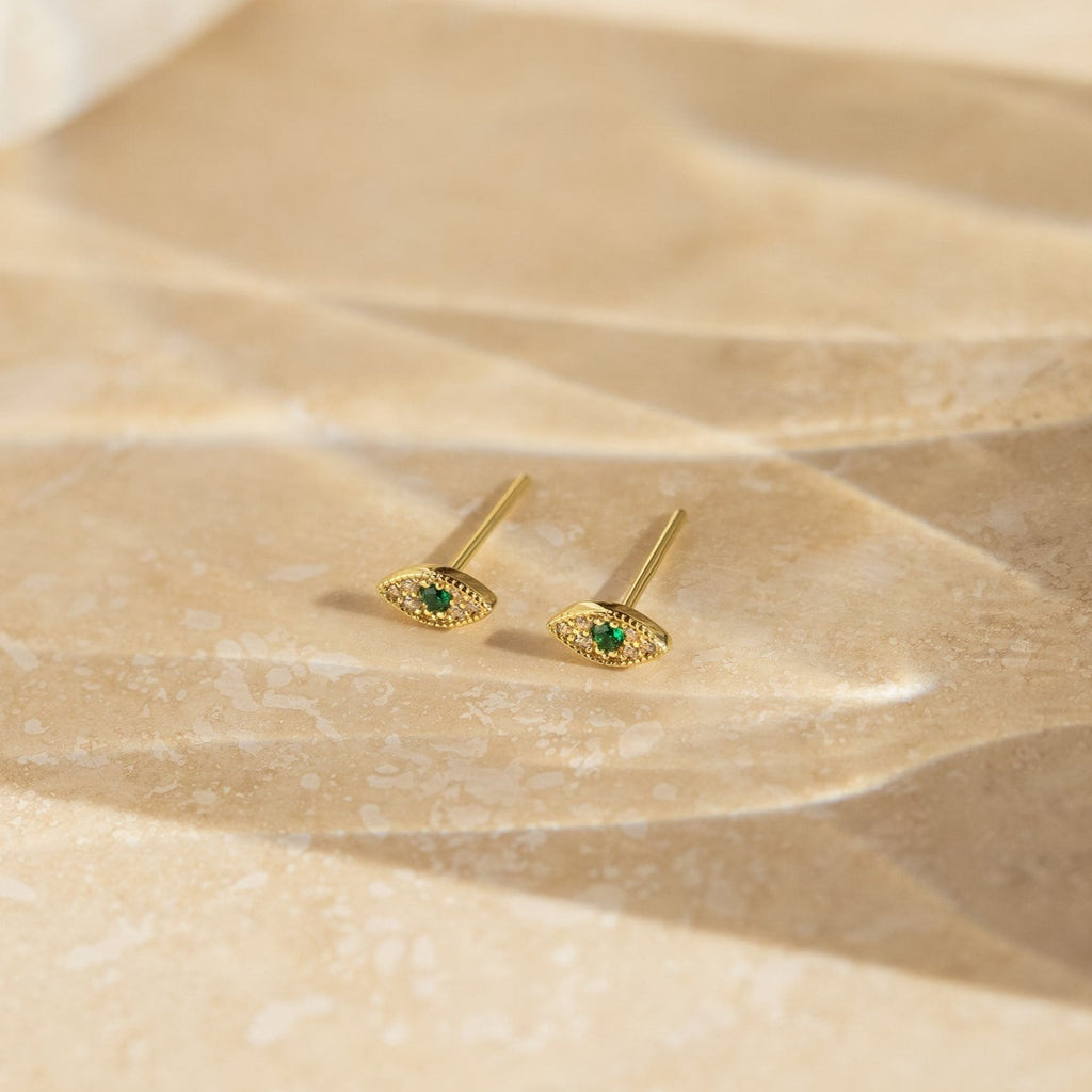 Haven Emerald Eye Studs showcased on a textured beige surface in soft lighting.