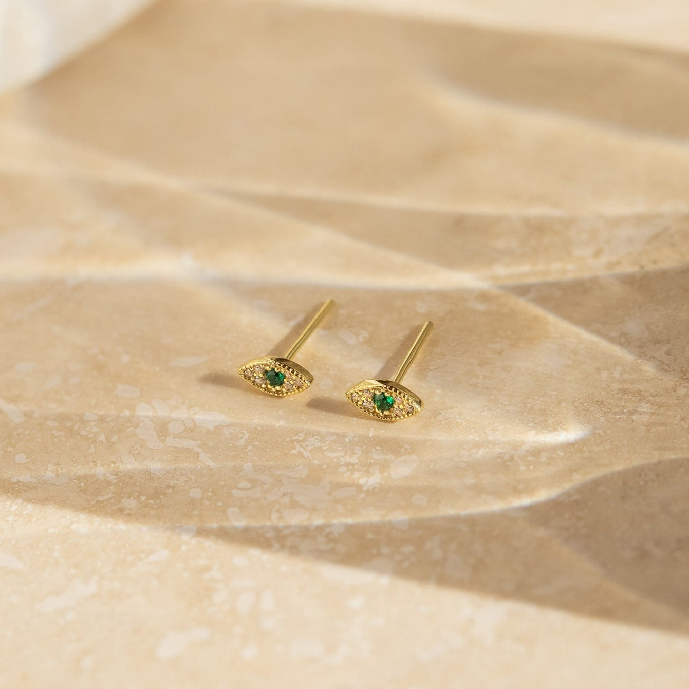 Haven Emerald Eye Studs showcased on a textured beige surface in soft lighting.