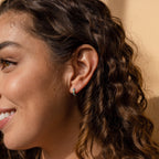 A woman with curly hair smiles brightly, her look enhanced by the Opal Inlay Huggies Set.