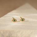 Haven Emerald Eye Studs featuring emerald stone centers and small clear stones, displayed on a light stone surface.