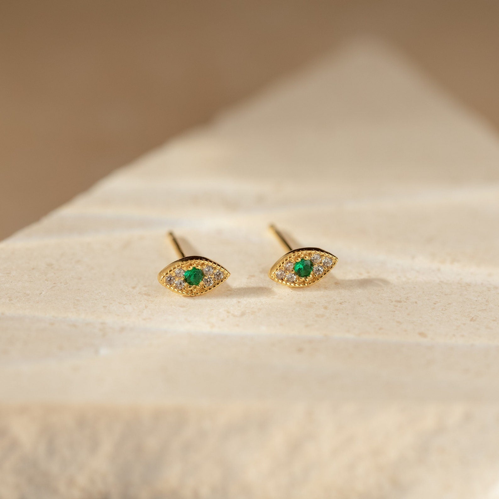 Haven Emerald Eye Studs featuring emerald stone centers and small clear stones, displayed on a light stone surface.