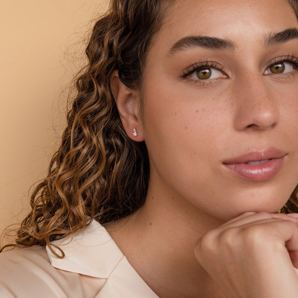 Woman with curly hair wears Flora Marquise Studs in Sterling Silver with a cream blouse, resting her chin on her hand and looking at the camera.
