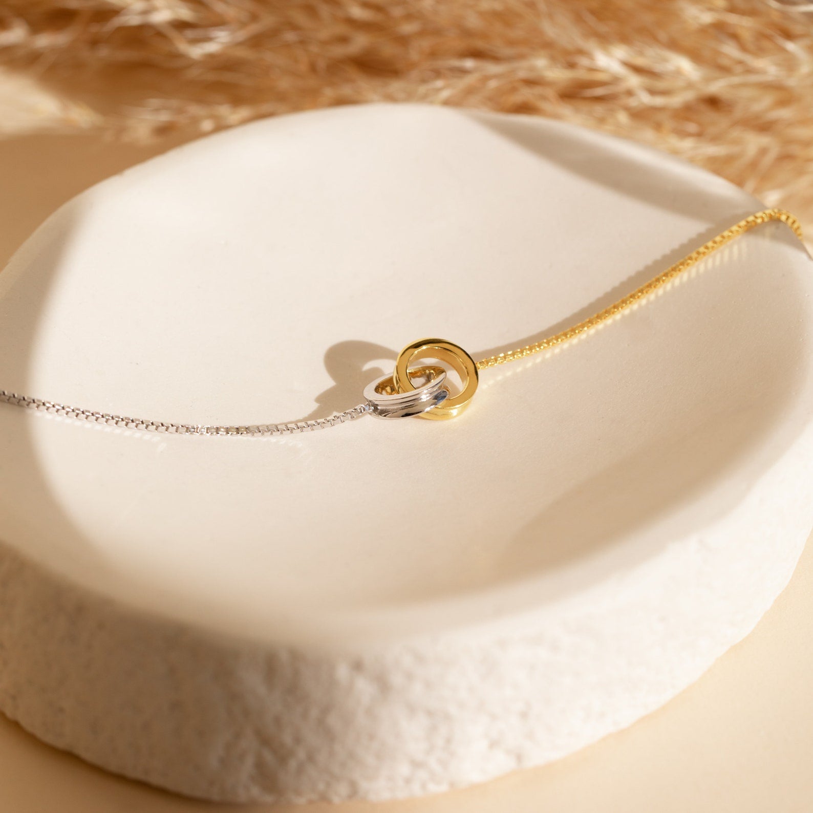 Elegant Interlocking Circles Bracelet in two-tone silver and gold—perfect for minimalist style or as a thoughtful anniversary gift, beautifully displayed on a white ceramic dish.