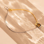 The Interlocking Circles Bracelet, featuring minimalist gold and silver rings, sits on a sunlit beige surface—an elegant anniversary gift.