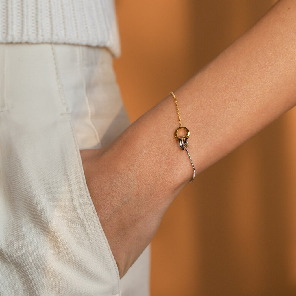 The Interlocking Circles Bracelet in gold and silver features minimalist circular charms, elegantly adorning the wrist—an ideal anniversary gift for someone special.