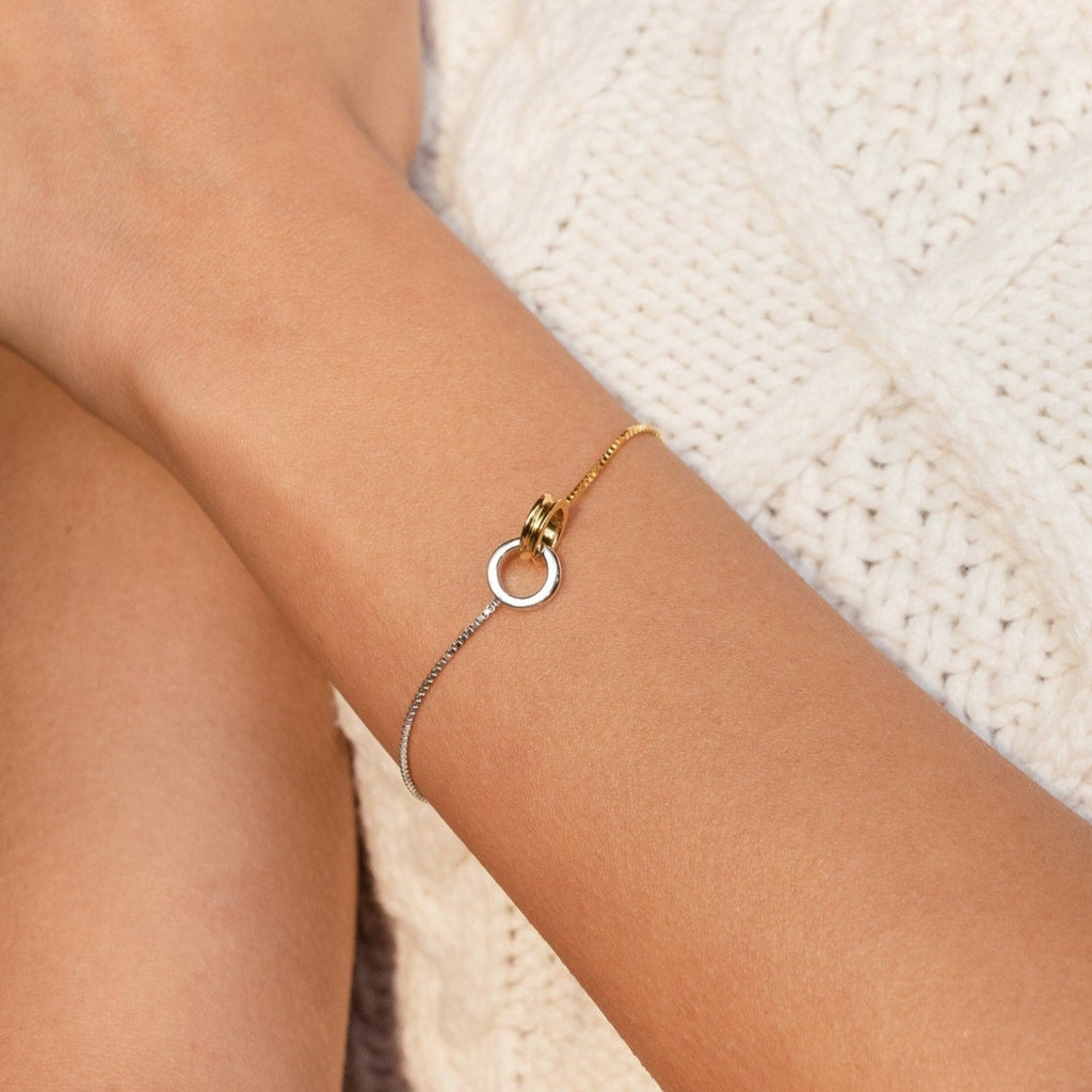 Close-up of a wrist wearing the Interlocking Circles Bracelet—a minimalist piece featuring a circular pendant—set against a cream knit sweater.