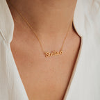 The Maine Kid's Name Necklace features the name Stella and a star charm, shown worn over a white shirt—an adorable personalized gold piece of kids jewelry, perfect for any occasion.