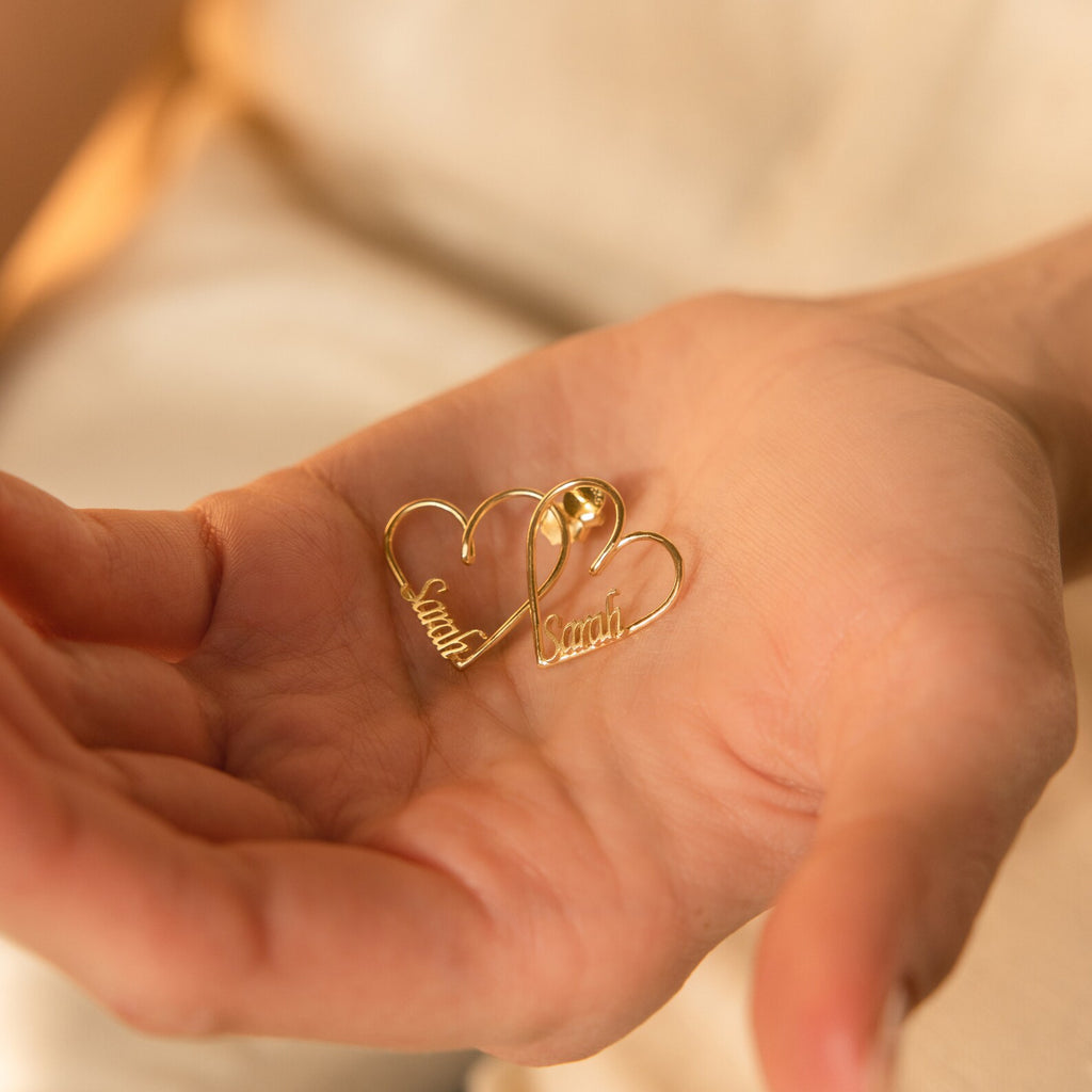 A hand holds two gold London Heart Name Earrings, each featuring the name Sarah inside—an ideal personalized gift.