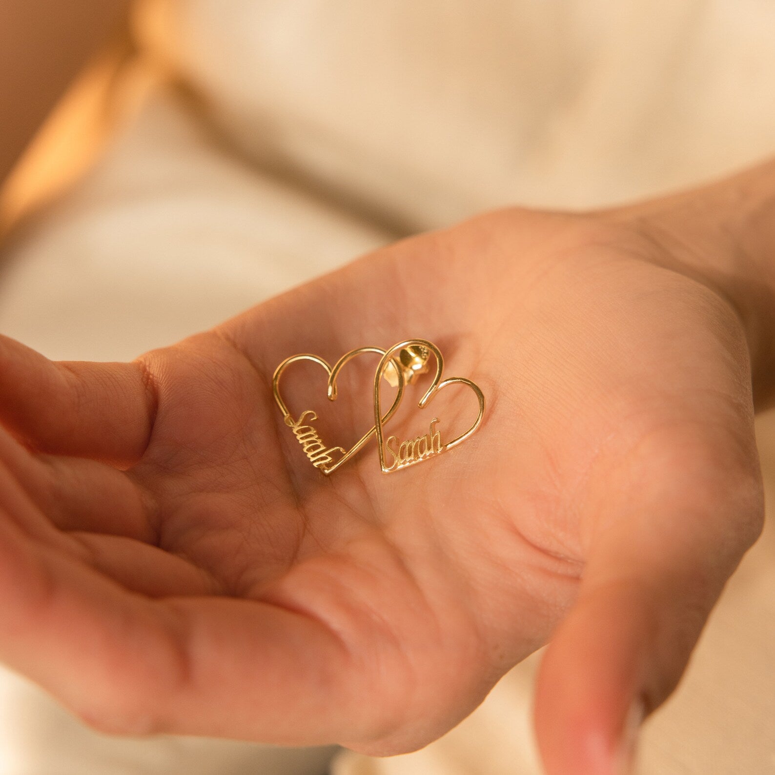 A hand holds two gold London Heart Name Earrings, each featuring the name Sarah inside—an ideal personalized gift.