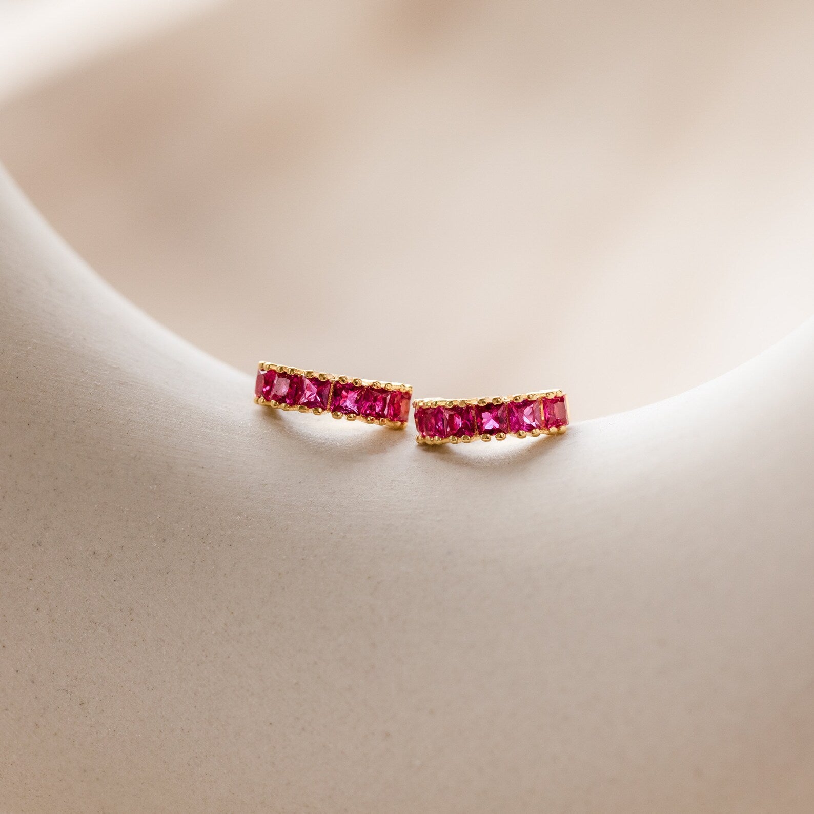 The Genevieve Birthstone Huggies in Ruby (July) are shown on a light, smooth surface—making them a charming gift for mom.