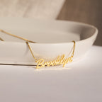 Casella Name Necklace in Box Chain showcases "Brooklyn" in a delicate script, elegantly displayed on the edge of a white dish—perfect as a custom gift for any occasion.