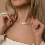 A woman wearing a white top holds the Butterfly Name Necklace in Box Chain, personalized with the name Teagan and adorned with a delicate butterfly charm.