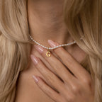 A woman with long blonde hair and manicured nails wears the Newsletter Pearl Initial Necklace, showcasing a customizable letter charm—a perfect example of minimalist jewelry.