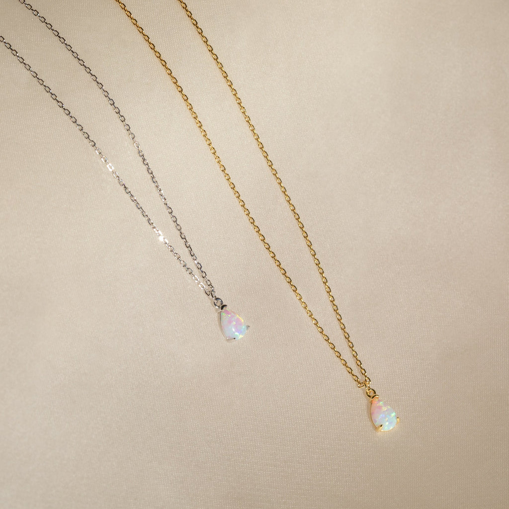 Two teardrop opal charm pendants on gold and silver chains rest on beige fabric—an elegant Tabitha Opal Drop Necklace, perfect as a romantic gift.