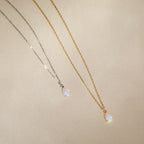 Two teardrop opal charm pendants on gold and silver chains rest on beige fabric—an elegant Tabitha Opal Drop Necklace, perfect as a romantic gift.