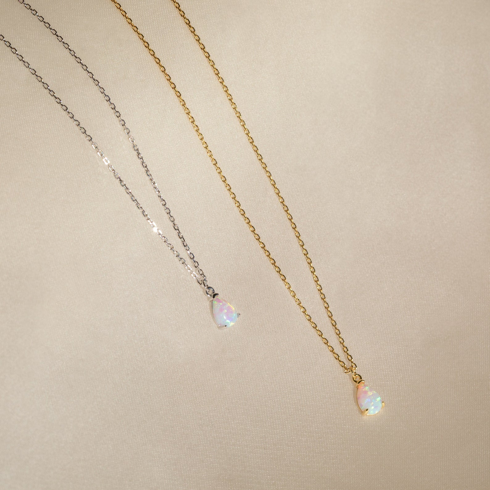 Two teardrop opal charm pendants on gold and silver chains rest on beige fabric—an elegant Tabitha Opal Drop Necklace, perfect as a romantic gift.