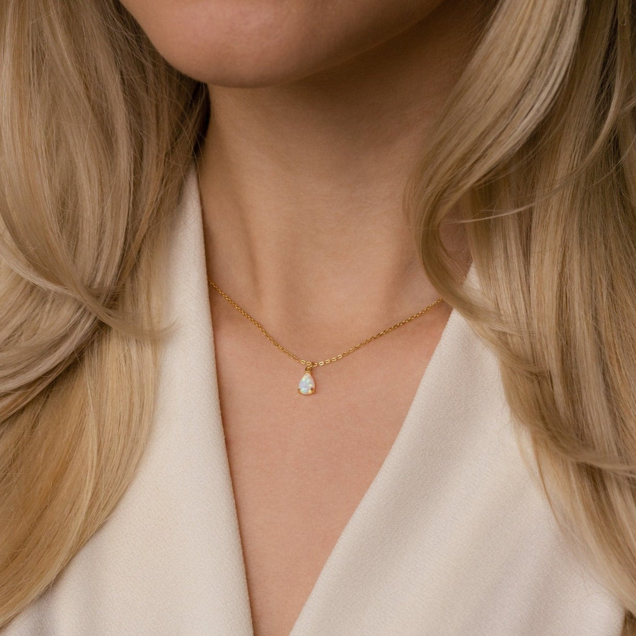A woman wears the Tabitha Opal Drop Necklace, featuring a delicate teardrop charm and paired with a cream blouse—an elegant piece that's perfect as a romantic gift.