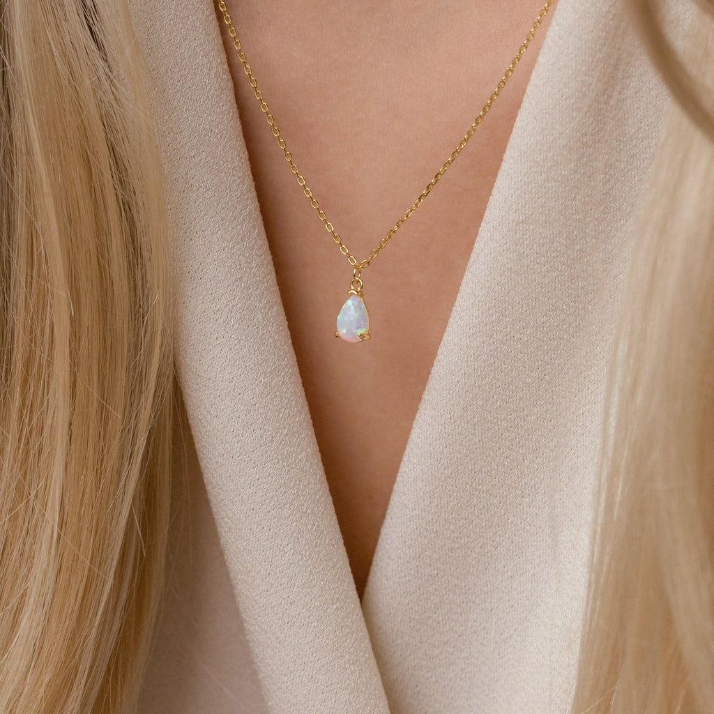 The Tabitha Opal Drop Necklace with a teardrop charm rests delicately against a beige V-neck top, making it a thoughtful romantic gift.