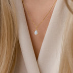 The Tabitha Opal Drop Necklace with a teardrop charm rests delicately against a beige V-neck top, making it a thoughtful romantic gift.