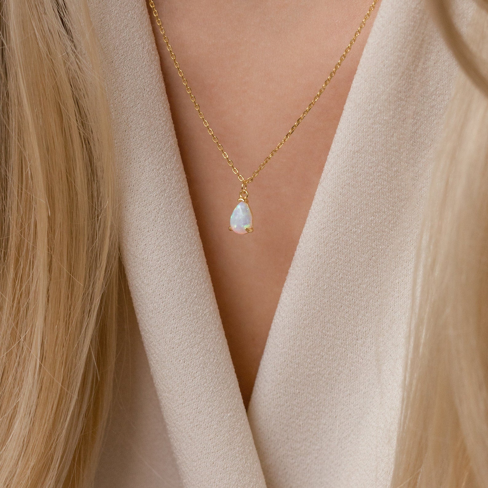The Tabitha Opal Drop Necklace with a teardrop charm rests delicately against a beige V-neck top, making it a thoughtful romantic gift.