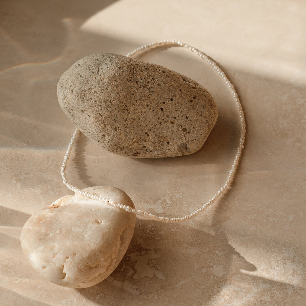 Flat lay of dainty off white freshwater pearl necklace with petite, irregularly shaped pearls, organic texture. 