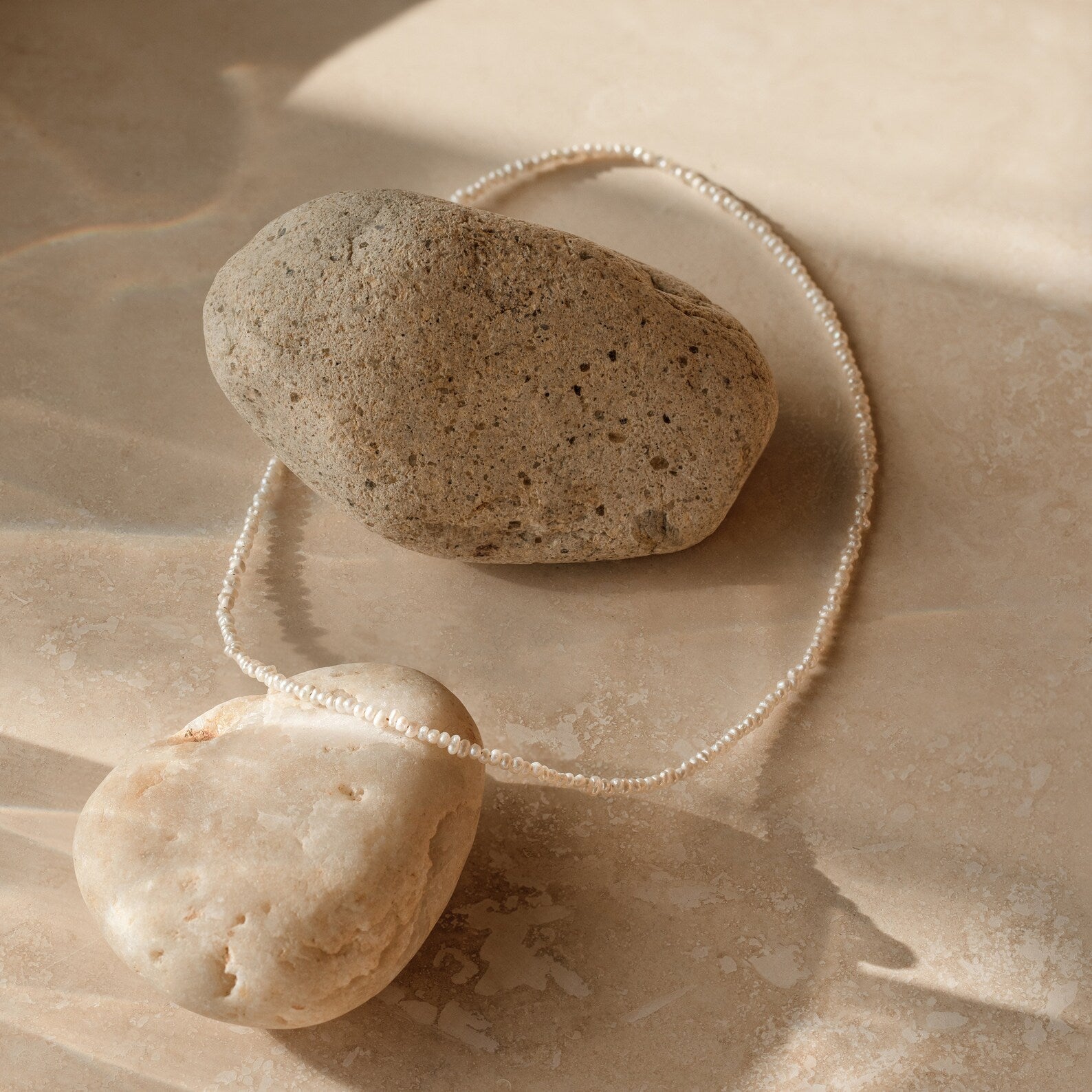 Flat lay of dainty off white freshwater pearl necklace with petite, irregularly shaped pearls, organic texture. 