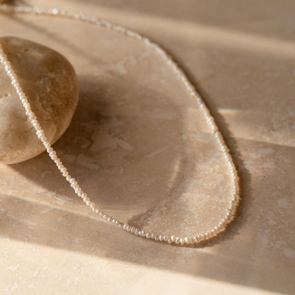  Flat-lay image of the pearl choker arranged in an oval on a beige surface, highlighting the dainty chain and irregular freshwater pearls.