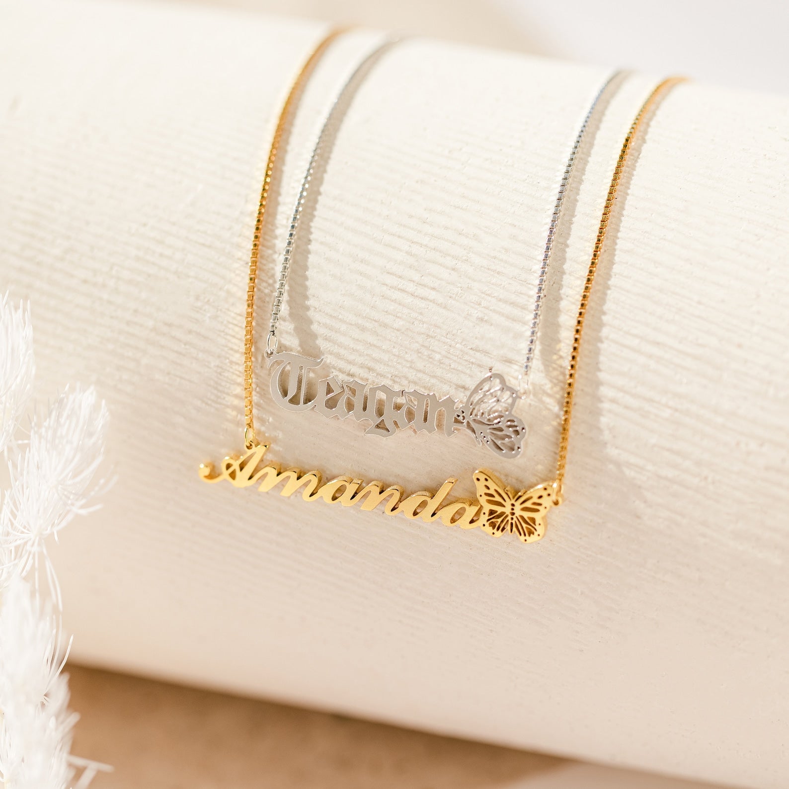 The Butterfly Name Necklace in Box Chain is shown in gold and silver variants with butterfly charms on a cream surface—ideal as a personalized necklace or unique name pendant.